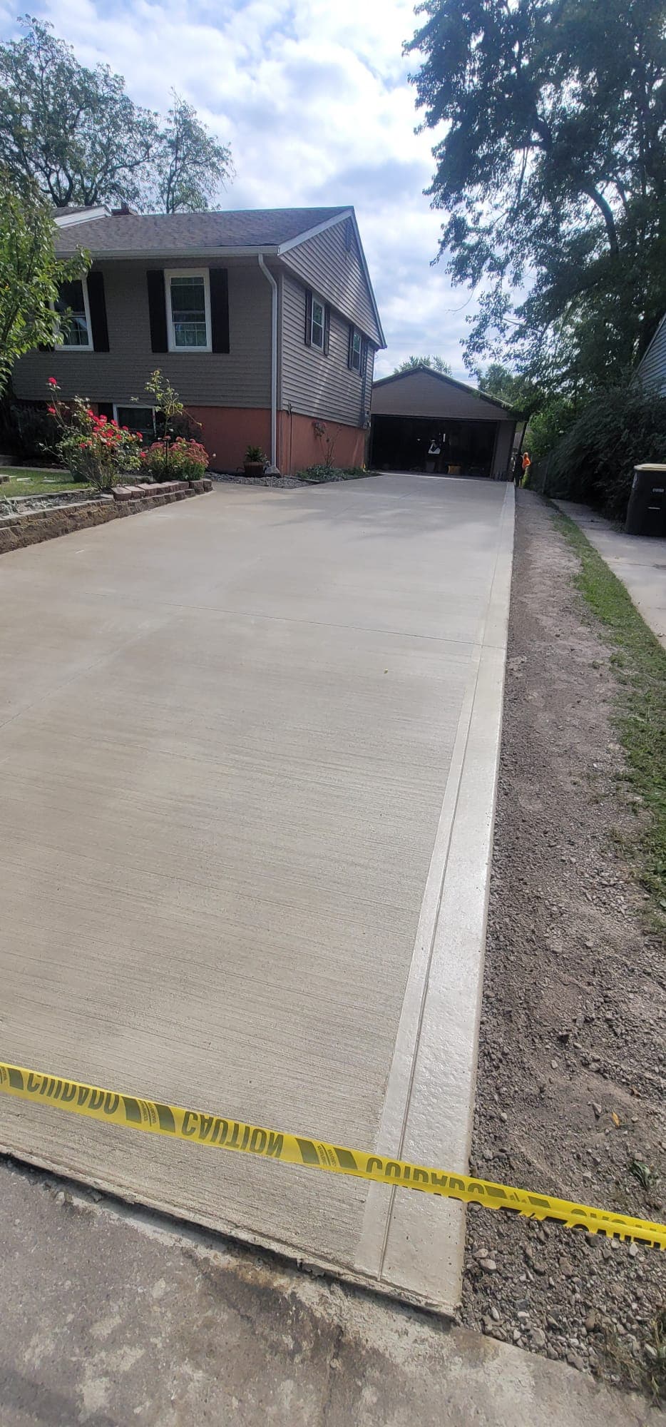 Full driveway approach from the street to the rear garage, with caution tape across the newly placed concrete.
