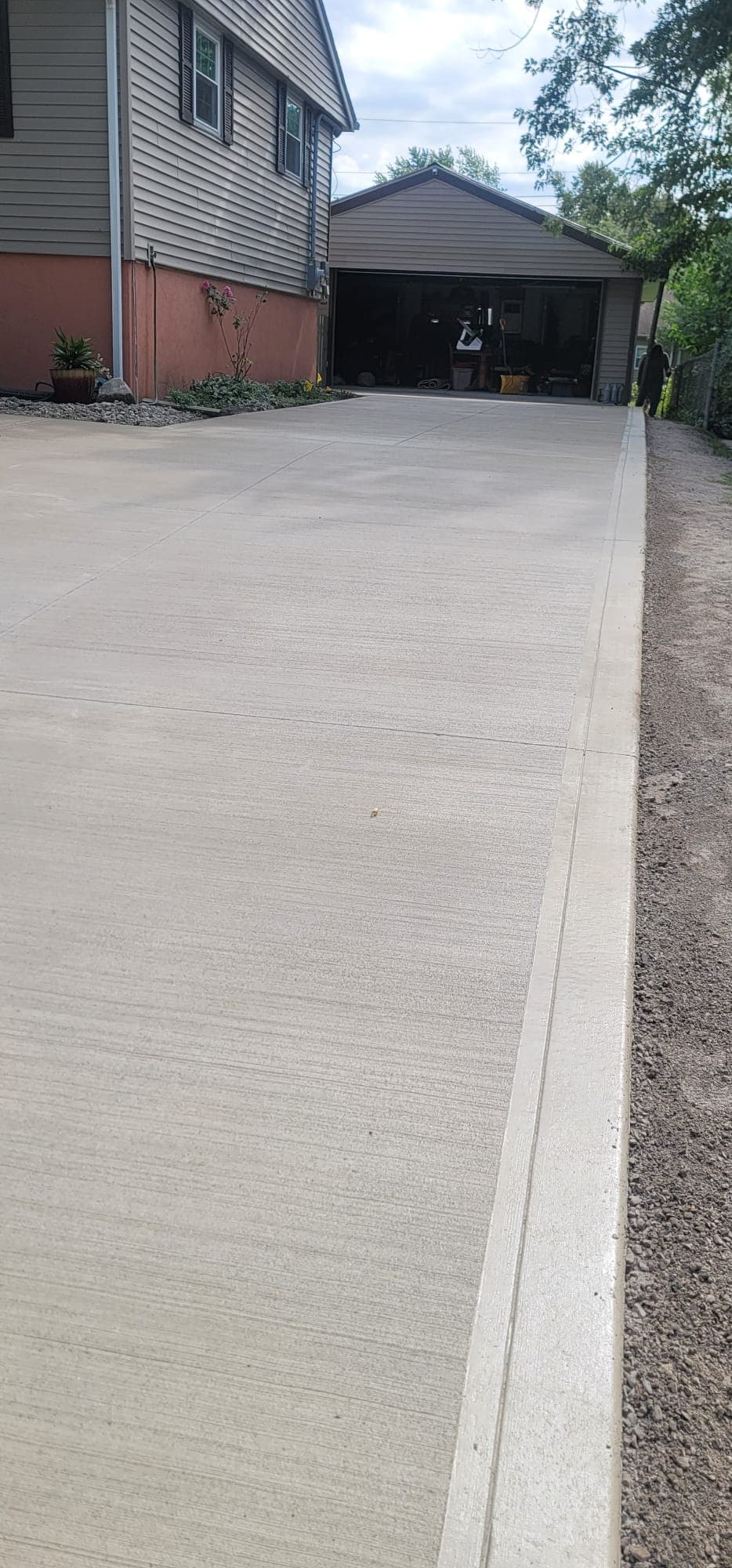 Broom-finished concrete driveway with straight joints and a smooth edge strip, leading beside a house to a detached garage.