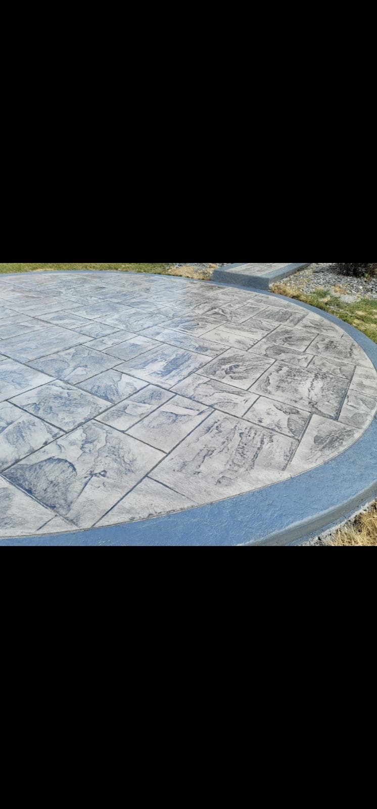 Close view of rectangular stamp impressions and mottled gray texture meeting the blue-gray border of a circular concrete patio.
