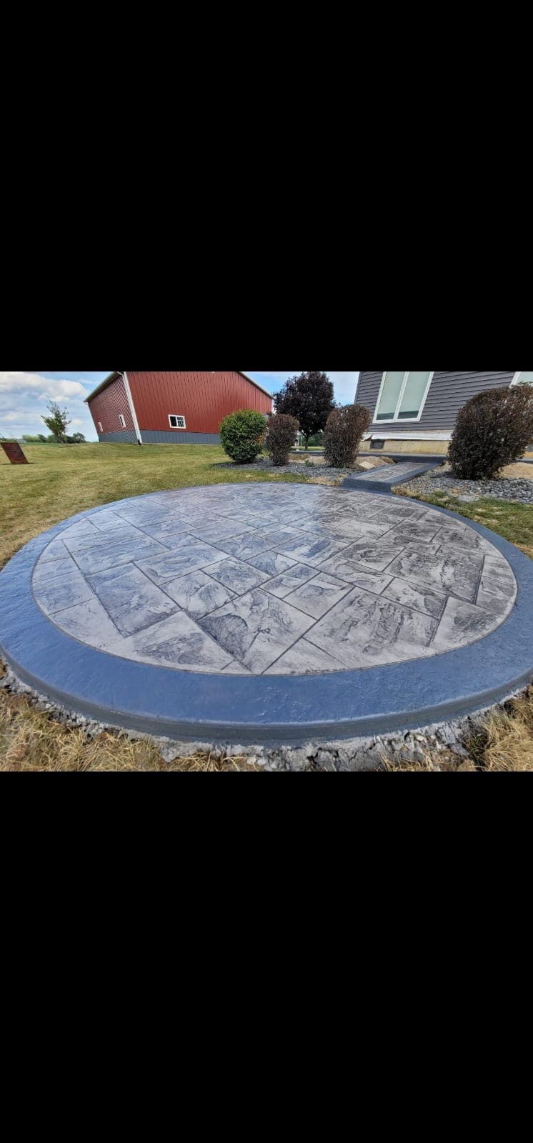 Circular gray stamped concrete patio with a broad blue-gray border and a short connecting walkway toward the house.