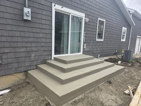 Broad rectangular concrete steps descending from a sliding back door to an unfinished yard.