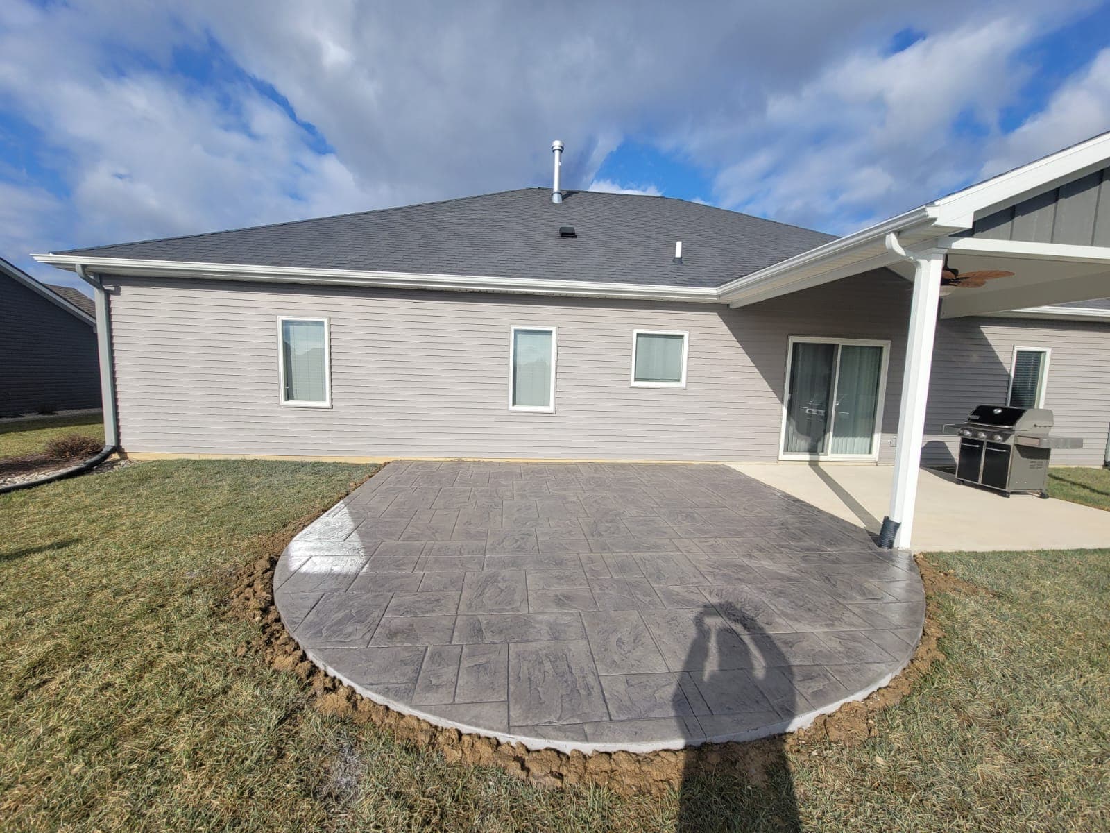 Gray stamped concrete patio with a rounded front edge adjoining a house and covered patio area.